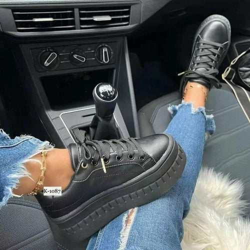 Casual platform women's sneakers worn in a car, showcasing black design and stylish look with ripped jeans.