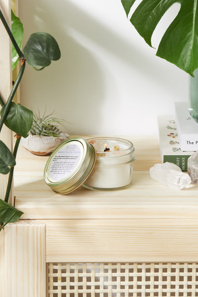 Space clearing intention candle shown on a wooden shelf with plants and decor.
